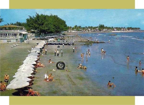 Foto tomada en algún momento de la segunda mitad de la década de 1960. La estructura que está en la orilla del mar (entre las sombrillas y las casuarinas), antes era una palapa con cubierta de palma.
